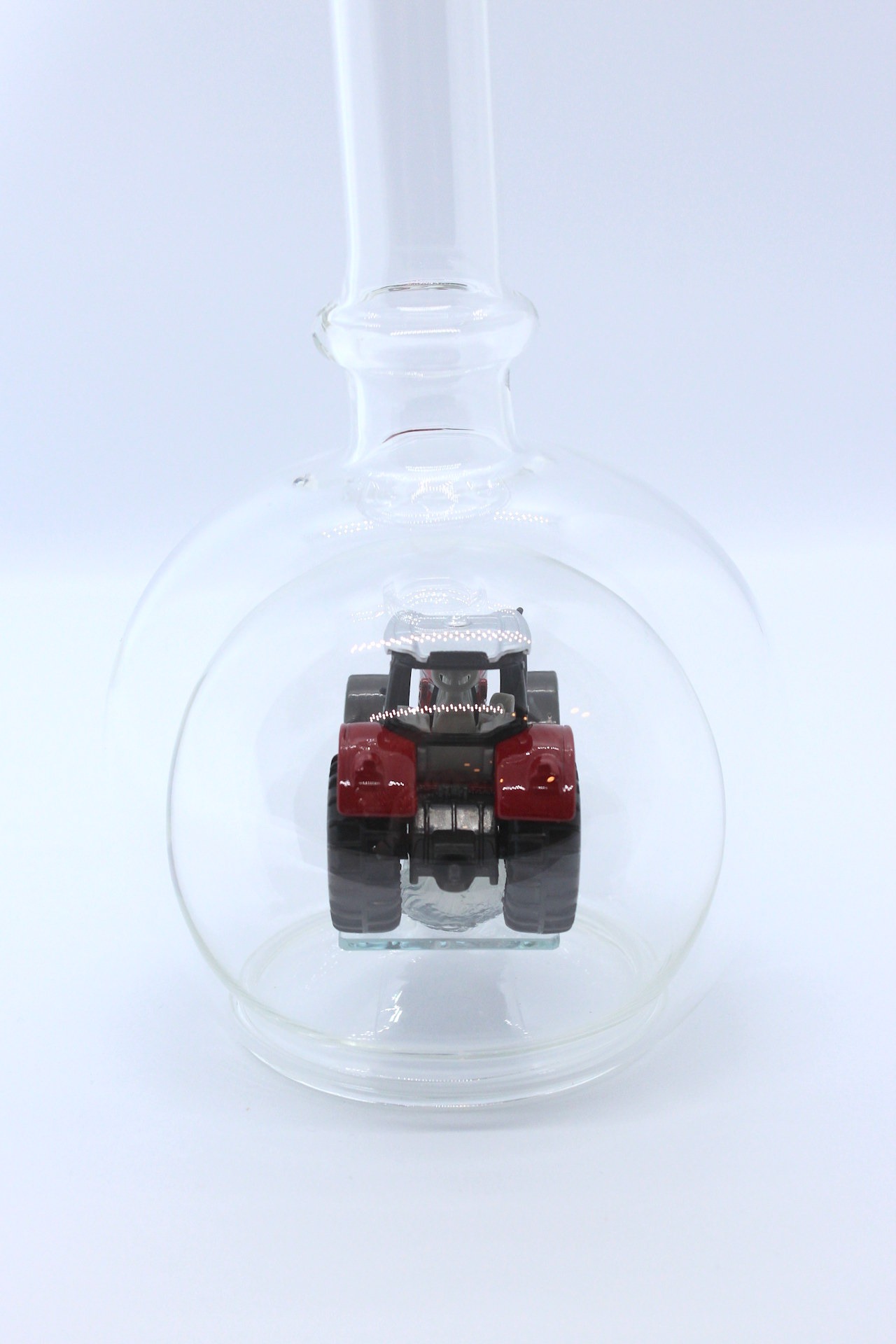 Eine leere bauchige Flasche aus Glas mit einem Massey-Ferguson-Traktor im Inneren.