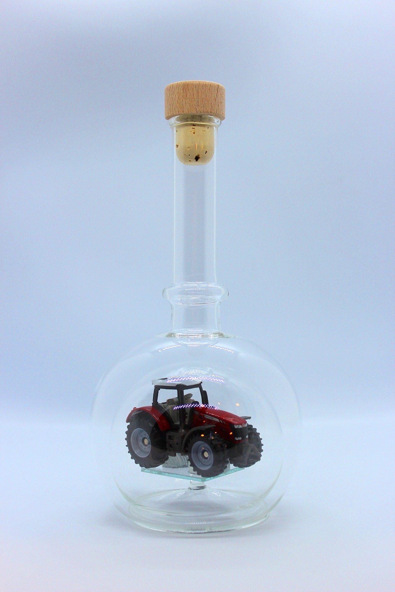 Eine leere bauchige Flasche aus Glas mit einem Massey-Ferguson-Traktor im Inneren.