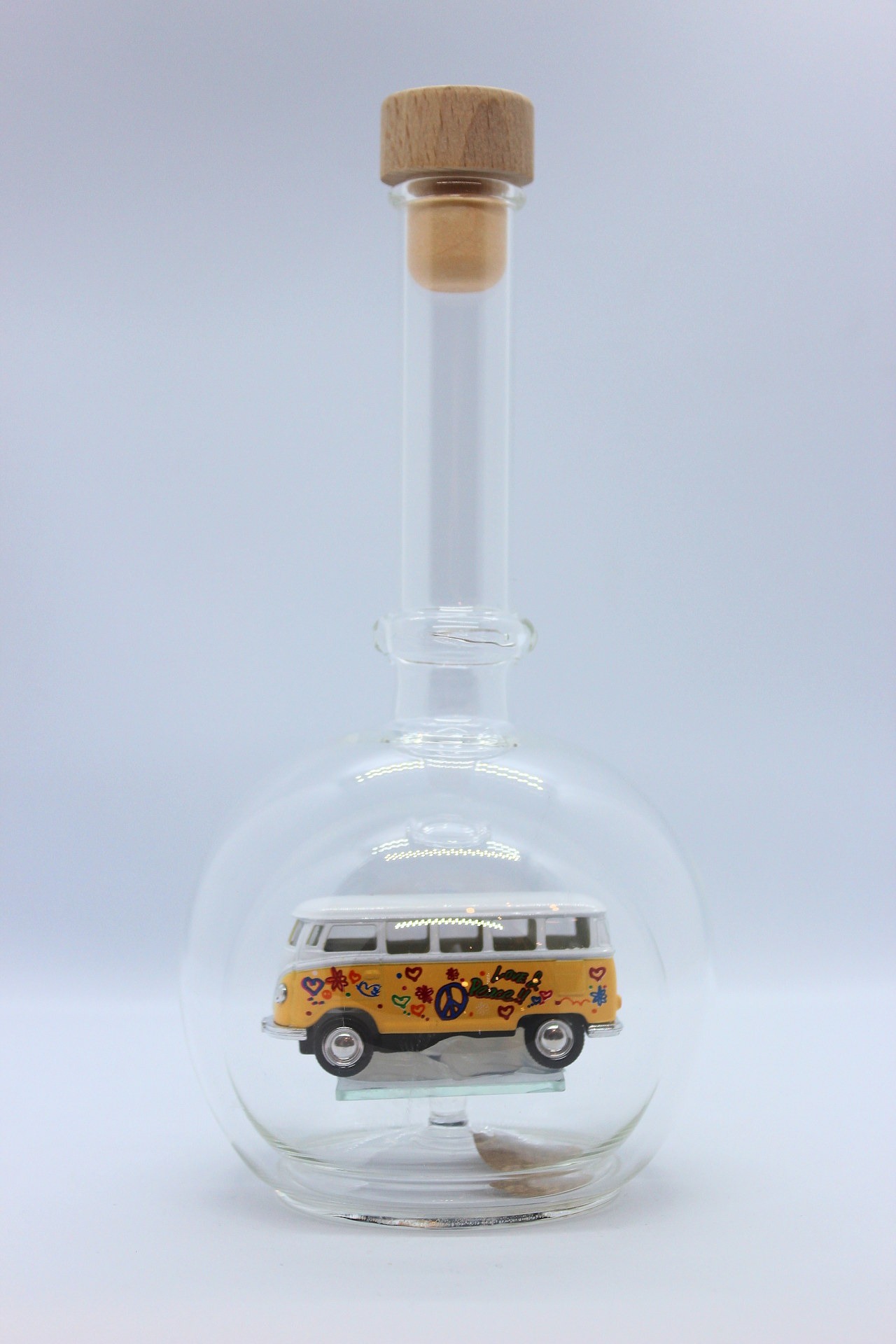 Eine leere bauchige Flasche aus Glas mit einem VW Bus T1 Flower in gelb im Inneren.