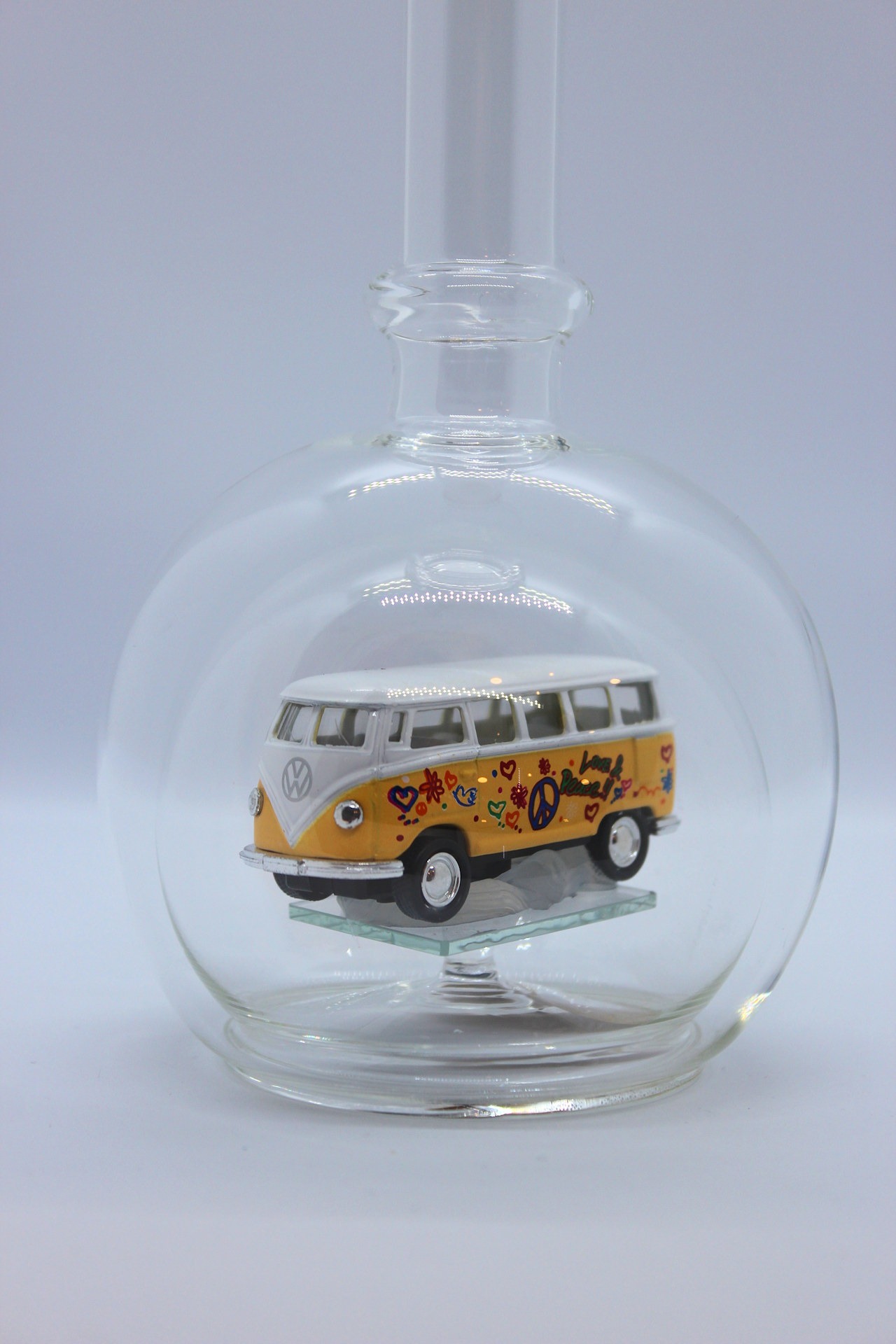 Eine leere bauchige Flasche aus Glas mit einem VW Bus T1 Flower in gelb im Inneren.