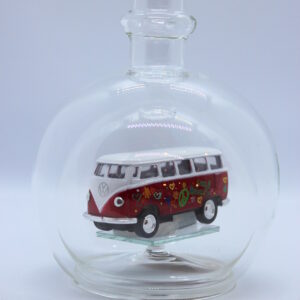 Eine leere bauchige Flasche aus Glas mit einem VW Bus T1 Flower in rot im Inneren.