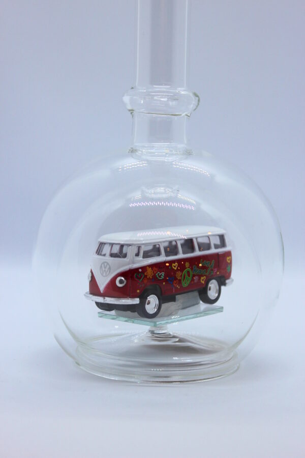 Eine leere bauchige Flasche aus Glas mit einem VW Bus T1 Flower in rot im Inneren.