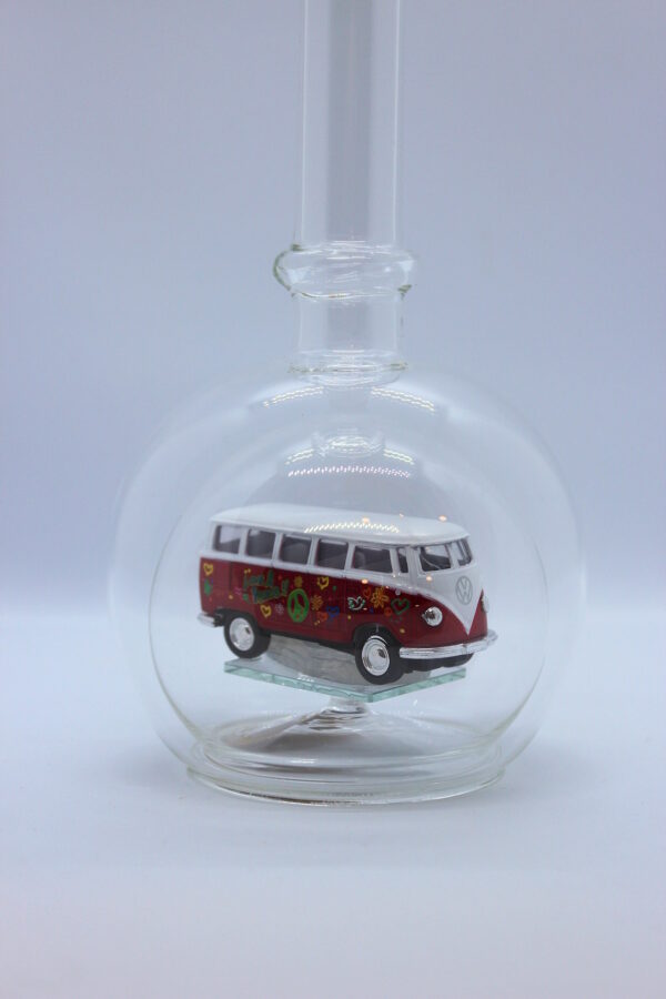Eine leere bauchige Flasche aus Glas mit einem VW Bus T1 Flower in rot im Inneren.