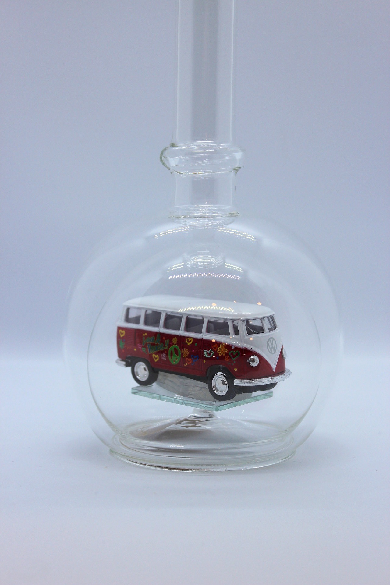 Eine leere bauchige Flasche aus Glas mit einem VW Bus T1 Flower in rot im Inneren.