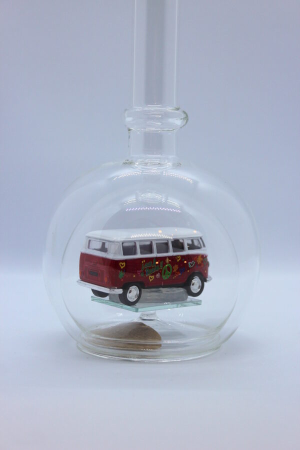 Eine leere bauchige Flasche aus Glas mit einem VW Bus T1 Flower in rot im Inneren.