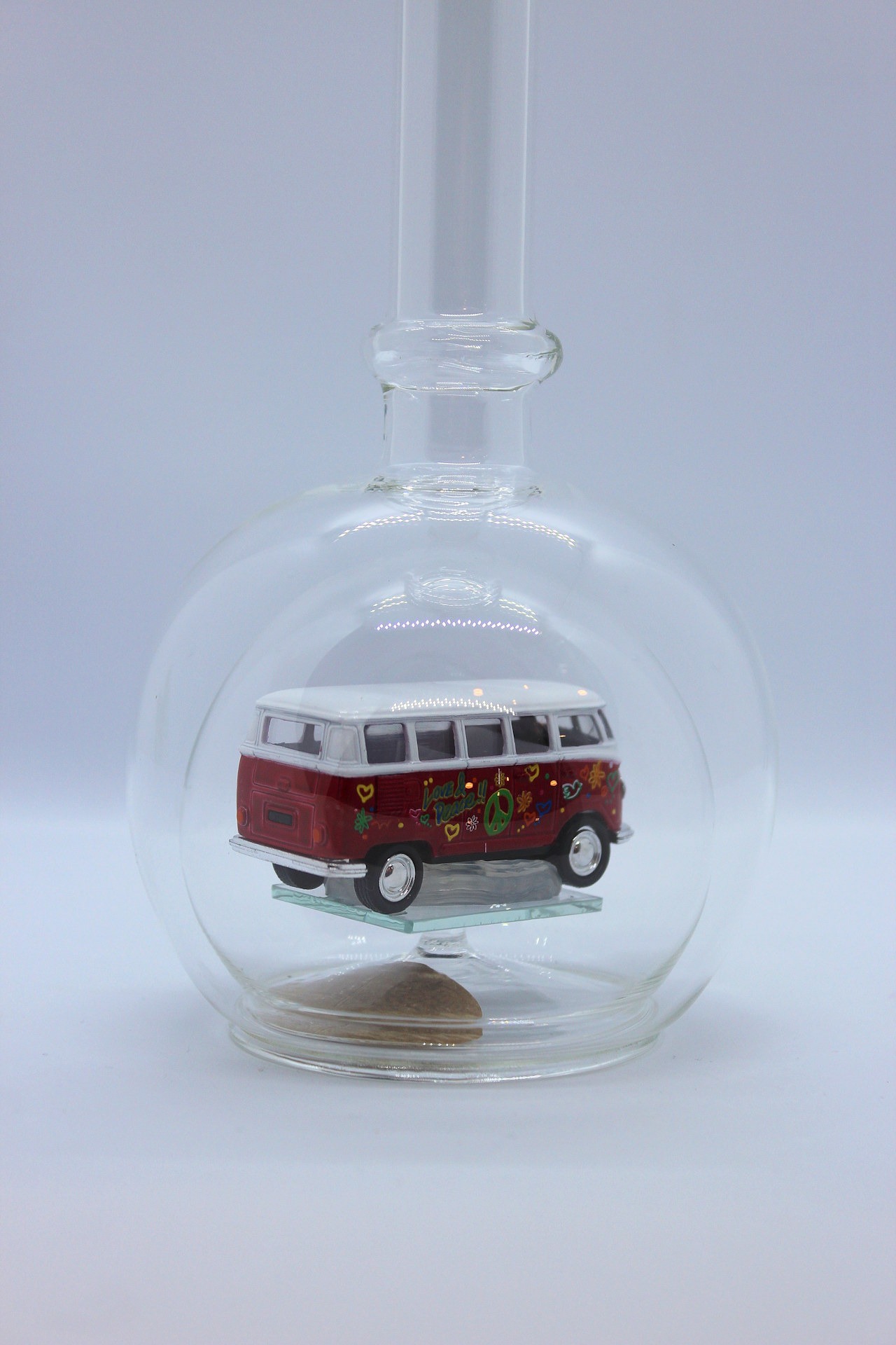 Eine leere bauchige Flasche aus Glas mit einem VW Bus T1 Flower in rot im Inneren.