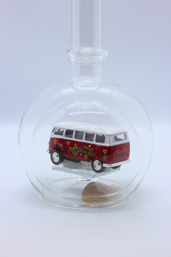 Eine leere bauchige Flasche aus Glas mit einem VW Bus T1 Flower in rot im Inneren.
