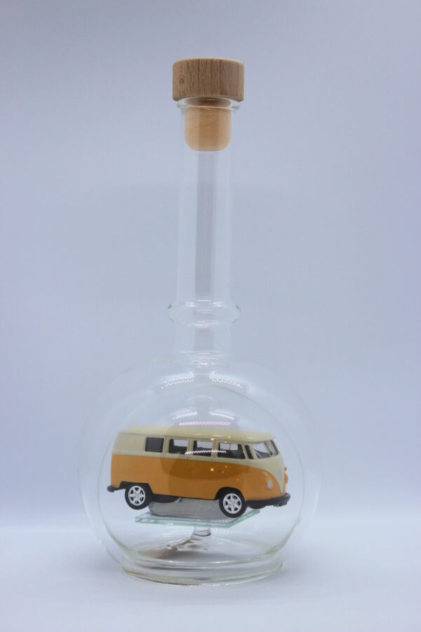 Eine leere bauchige Flasche aus Glas mit einem VW Bus T1 Samba in gelb im Inneren.