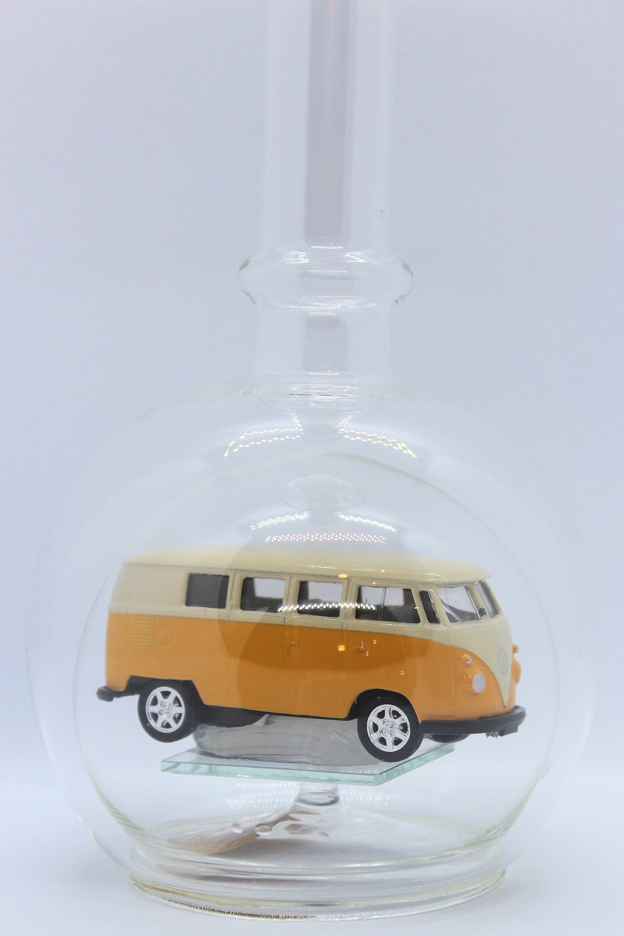 Eine leere bauchige Flasche aus Glas mit einem VW Bus T1 Samba in gelb im Inneren.