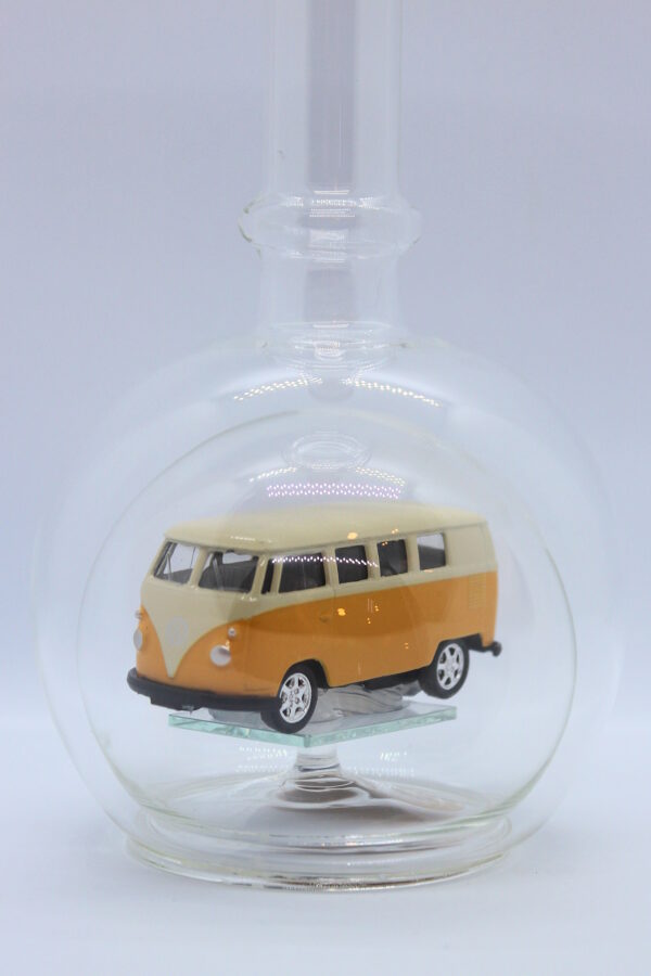 Eine leere bauchige Flasche aus Glas mit einem VW Bus T1 Samba in gelb im Inneren.