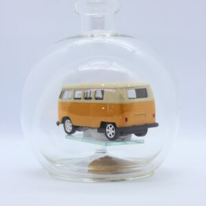 Eine leere bauchige Flasche aus Glas mit einem VW Bus T1 Samba in gelb im Inneren.