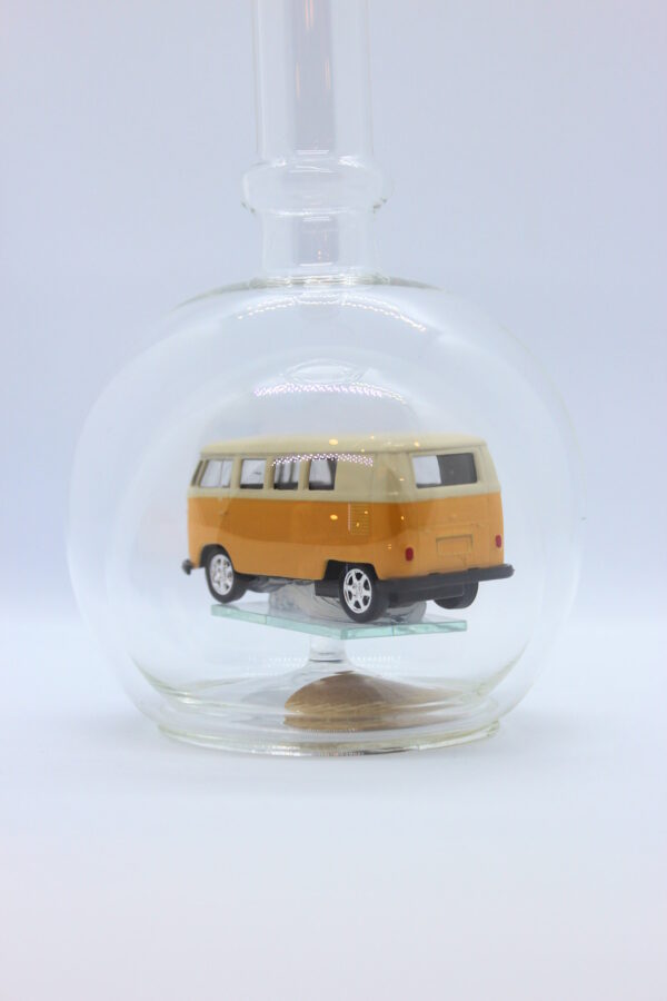 Eine leere bauchige Flasche aus Glas mit einem VW Bus T1 Samba in gelb im Inneren.