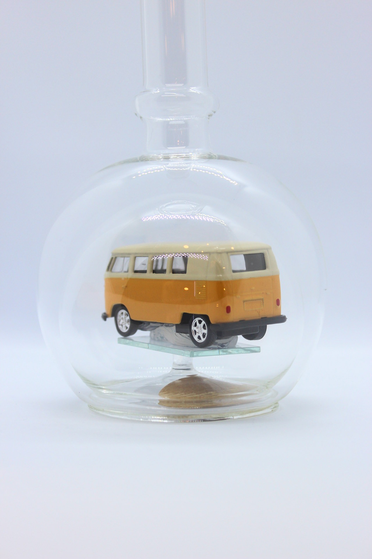 Eine leere bauchige Flasche aus Glas mit einem VW Bus T1 Samba in gelb im Inneren.