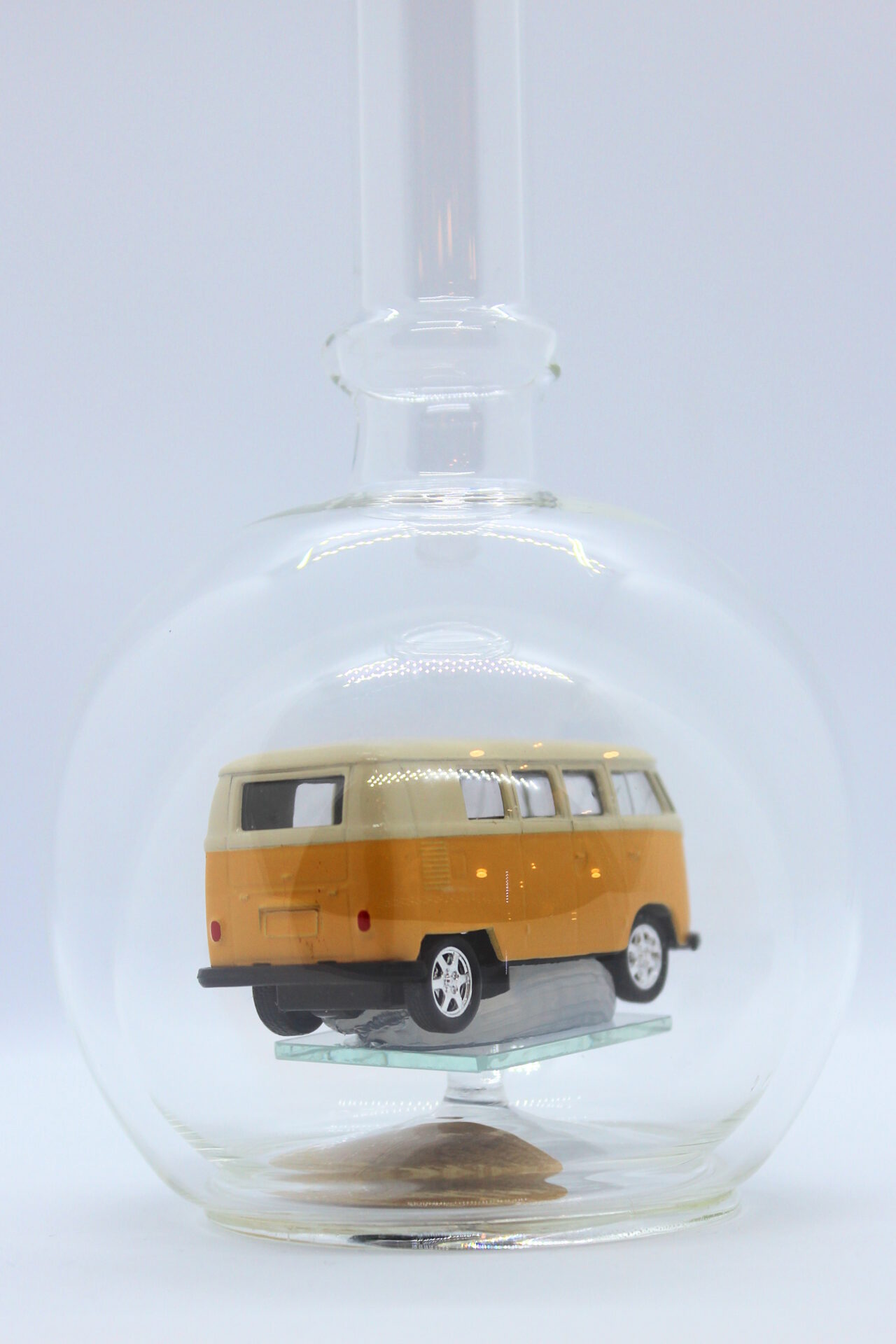 Eine leere bauchige Flasche aus Glas mit einem VW Bus T1 Samba in gelb im Inneren.