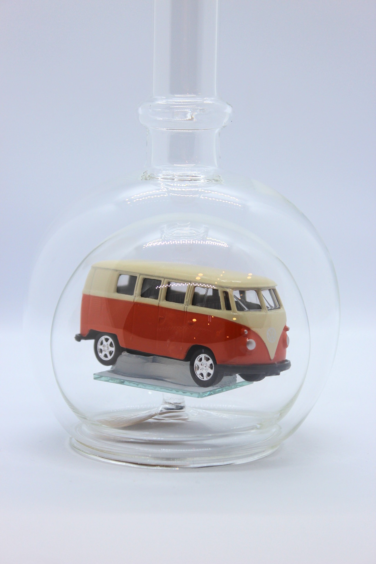 Eine leere bauchige Flasche aus Glas mit einem VW Bus T1 Samba in orange im Inneren.