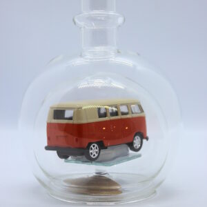 Eine leere bauchige Flasche aus Glas mit einem VW Bus T1 Samba in orange im Inneren.