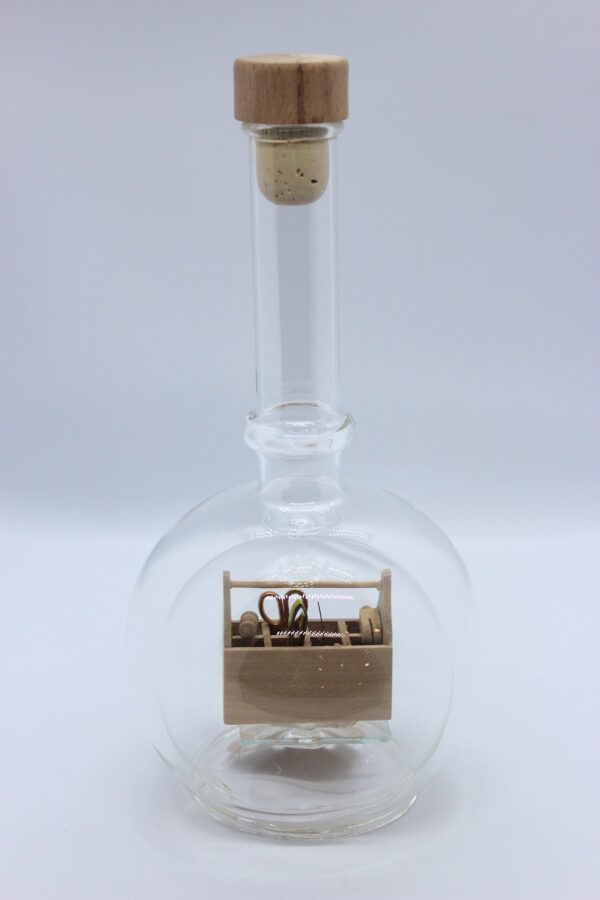 Eine leere bauchige Flasche aus Glas mit einem Werkzeugkasten Holz im Inneren.
